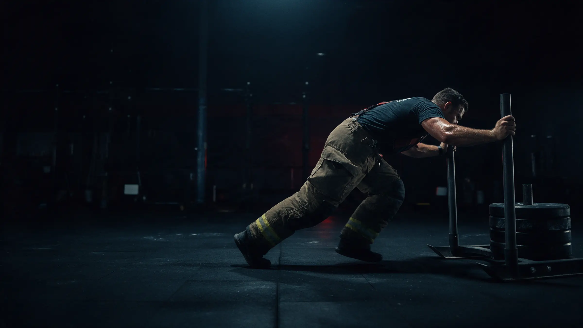 A firefighter driving a weighted sled across a gym floor.